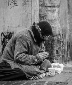 grayscale photography of man praying on sidewalk with food in front