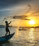 person throwing fish net while standing on boat
